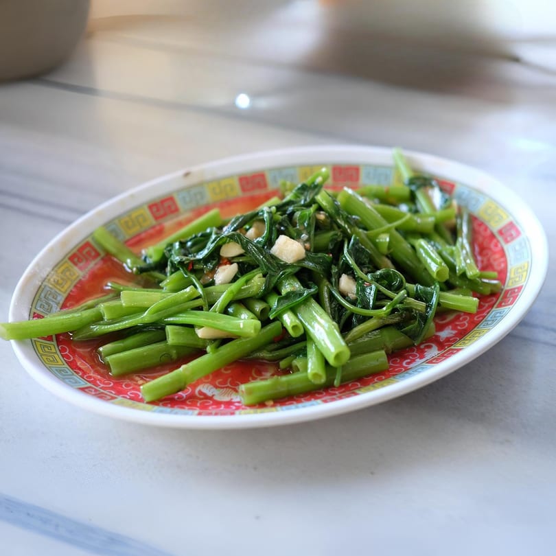 Asian stir-fried green vegetables with garlic and chili on a red and white patterned plate.