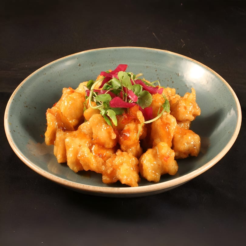 Crispy Asian-style chicken pieces coated in a sweet orange sauce, garnished with fresh greens and red onions.