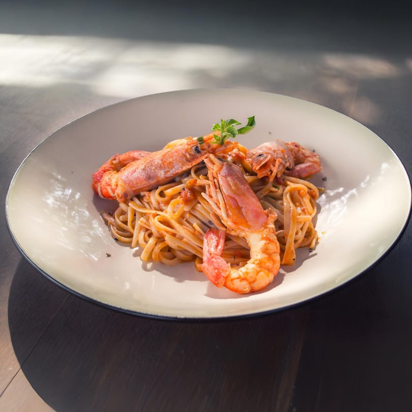 Shrimp linguine pasta with fresh herbs on a white plate, bathed in natural sunlight.