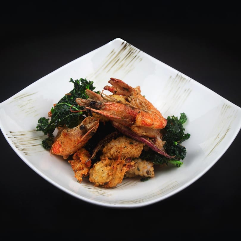 Crispy fried shrimp and calamari with dark green leafy vegetables on a white square plate.